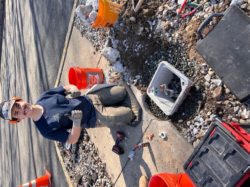 Crew member giving a thumbs-up while wiring an in-ground junction box